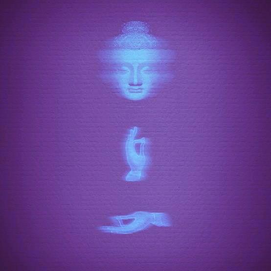 image of buddha in blue with hand in mudra revealed through purple background